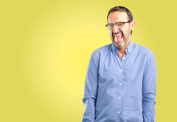 Handsome middle age man sticking out tongue at camera at sign of disobedience, protest and...