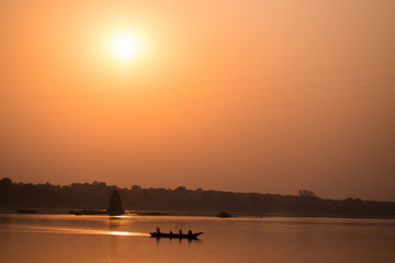 Sunset reflection on river, orange toned, dark silhouette.