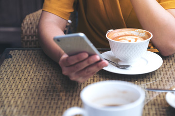 Closeup image of a woman using and looking at smart phone with coffee cups in cafe