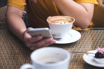 Closeup image of a woman using and looking at smart phone with coffee cups in cafe