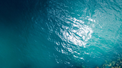 Aerial: overhead view of transparent blue sea surface against the coral line and bottom