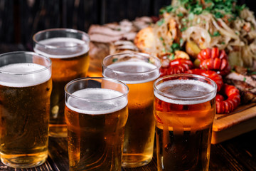 Five glasses of beer near the set of grilled meat on wood backro