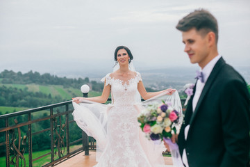 Wedding fashion portrait of young couple with nice boquet. Bride and groom in carpathians, mountains, beautiful nature, landscape, scenery. Newlyweds at mountain terrace. Windy veil. Tender picture.