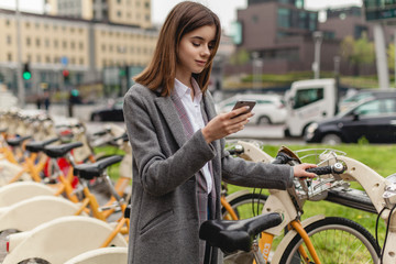 Young stylish woman using bicycle rent mobile app smiling outdoors, portrait of female manager...