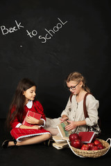 Naklejka premium two beautiful girlfriends schoolgirls sitting with books and a basket of apples on a black background
