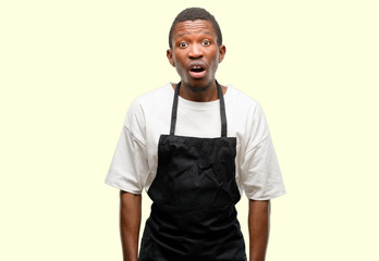 Fototapeta premium African man shop owner wearing apron scared in shock, expressing panic and fear