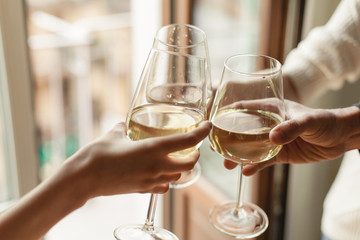 Young happy friends cheering with glasses of white wine, family dinning at home, enjoyment and party concept, best friends celebrating at home, traditional and holidays concept