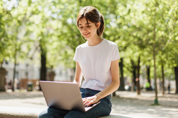 Young blogger using wireless connection to watch video in the park and talk via Skype with friends,...