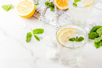 Summer refreshing drinks, mojito or lemonade with fresh mint, slices of lemon, ice, on a light background. copy space
