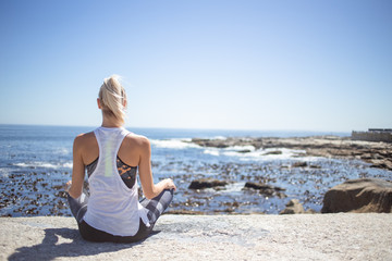 Fototapeta na wymiar Blond female fitness model meditating and doing yoga on a granite rock overlooking the ocean