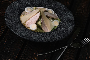 Salad with chicken, quail eggs and lettuce in plate on wood background