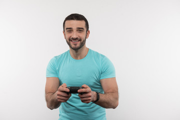 Interesting entertainment. Joyful bearded man holding a video game console while having fun at home