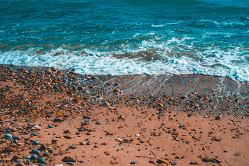 red colored sand beach with some small rocks and white waves