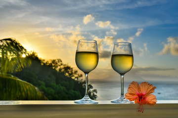 Romantic moments in summer at sunset with two glasses of white wine - Relaxing romantic holiday concept with beautiful view of tropical beach and coast