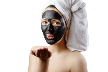  close-up portrait beautiful woman with facial black mask on white background, girl with a white towel on her head, satisfied and happy  smile, air kiss