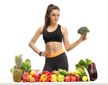 Fitness woman behind a table with fruit and vegetables holding broccoli