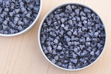The lead bullets are in a plastic round box for a air gun on wooden texture.