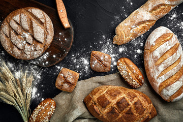 Homemade rye bread sprinkled with flour and various grains and seeds on a black background with...