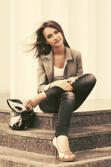 Happy young fashion woman in grey blazer and dark blue jeans sitting on steps