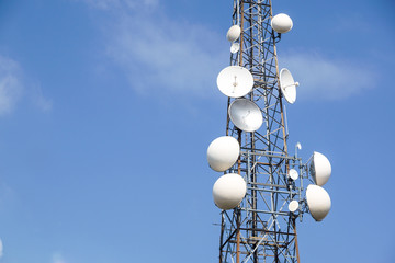 Mobile phone communication antenna tower with satellite dish on blue sky background,...