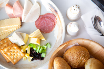 Breakfast with various of breads, cheese, ham, crakers, salami and pickles.