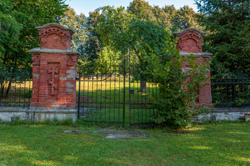 stara brama do parku przy cerkwi prawosławnej w Białowiezy. w oddali widać pasiekę z kilku kolorowych drewnianych uli - obrazy, fototapety, plakaty