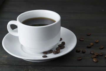 A cup of coffee, coffee beans on a dark wooden board.