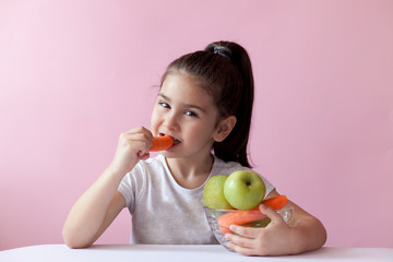 A cute little girl eating fresh vegetables. A portrait on а pastel background. Healthy teeth.