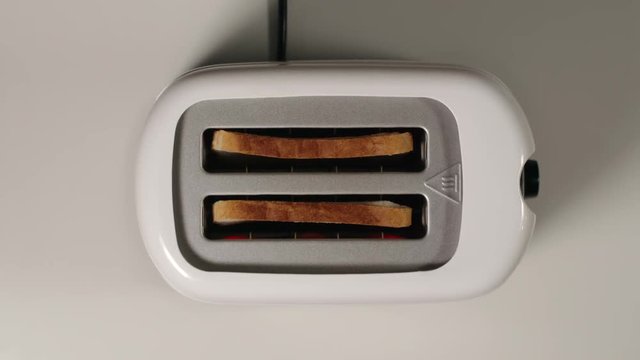 TOP VIEW: Roasted bread jump out from a white toaster on a white table
