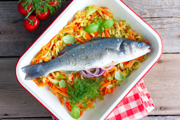 Raw fish seabass in enameled form for baking with courgettes and carrots, top view