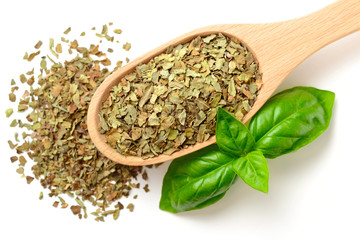 dried basil leaves in the wooden spoon, isolated on white, top view