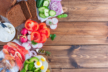 Ingredients for the preparation of a traditional Danish open sandwich called Smorrebrod on rye bread with vegetables, red fish, shrimps, eggs, herring and greens. Top view, horizontal, copy space.