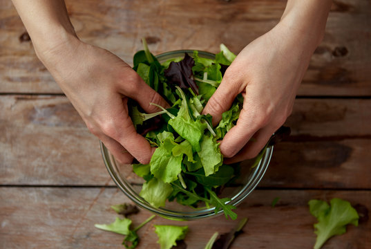 Closeup of woman hands cooking fresh green salad on wooden table in kitchen.