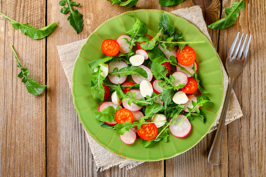 Vegetarian salad of arugula, tomato, radish and mozzarella cheese on an old wooden table.