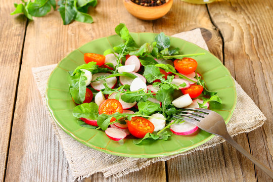 Vegetarian salad of arugula, tomato, radish and mozzarella cheese on an old wooden table.