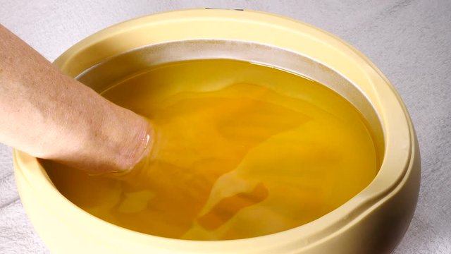 Close up slow motion shot of unrecognizable woman putting hand into paraffin bath taking care of hands skin.