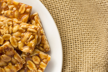 Candy with peanut: Pe de Moleque in Brazil and Chikki in India. Sweet food of Festa Junina, a typical brazilian party. Snacks on bowl and jute, burlap fabric.