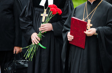 Two priests standing next to each other on the ceremony. One of them is holding flowers and another...