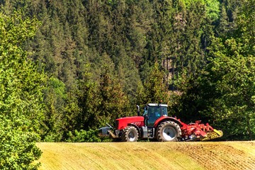 Field and operation of the tractor. Wind and dust over workers. Red tractor on a field....