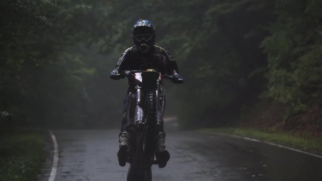 Shot of the Professional Motocross Driver Riding on His FMX Motorcycle on the rear wheel in the rain 4k