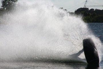 Wake Boarder Waterskiing Leaning Low Touching Water Creating Spray Silhouetted Against Sparkling...