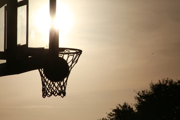 Basketball Hoop, Backboard and Net with Ball Swishing Through in Silhouette with Setting Sun Gleaming Through Directly Behind at Quiet Waters Park, Deerfield Beach, Florida