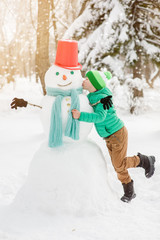 Happy little boy kissing snowman at sunset
