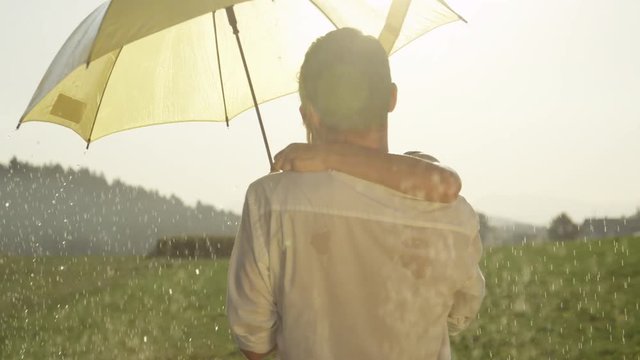 SLOW MOTION CLOSE UP LENS FLARE: Cute young couple kisses romantically in rural setting on a rainy summer afternoon. Happy woman and man dance and kiss on their date in the beautiful golden lit meadow