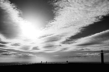 Sea view from the high shore with wooden fence. silhouettes of people and a monument on black and white photography