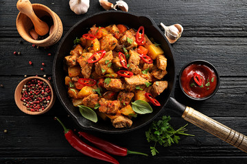 Traditional goulash stewed meat with potatoes, carrots and vegetables in a cast-iron frying pan on a dark wooden background. top view.