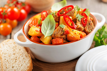 Traditional goulash stewed meat with potatoes, carrots and vegetables on a  wooden background. 