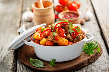 Traditional goulash stewed meat with potatoes, carrots and vegetables on a  wooden background. 