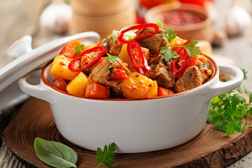 Traditional goulash stewed meat with potatoes, carrots and vegetables on a  wooden background. 