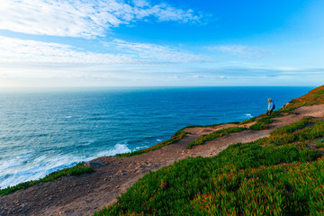 Fototapeta premium Sintra, Portugal 27 Jan, 2018 - man on high bank with green grass and hiking trails and a view of the blue sea